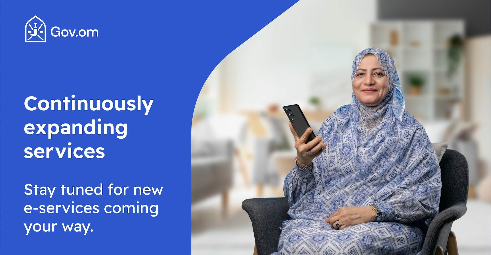 An older woman in a blue patterned hijab and dress is seated in a modern living room, holding a smartphone and smiling. The banner displays the Gov.om logo and the text: 'Continuously expanding services. Stay tuned for new e-services coming your way.'